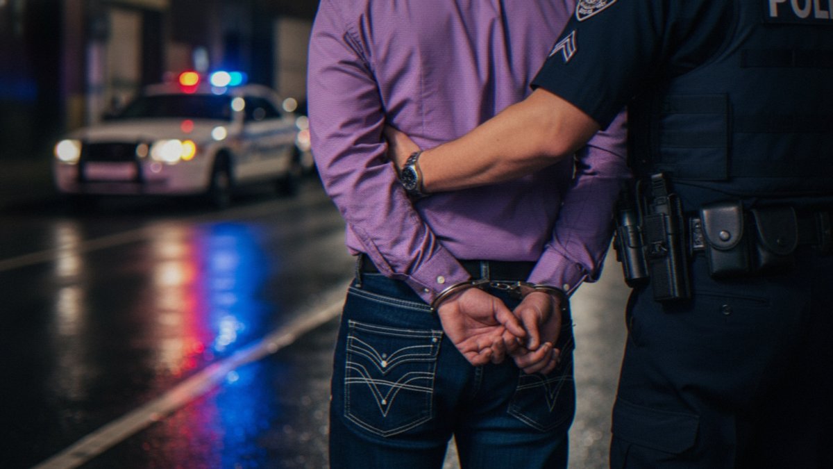 A suspect is escorted by law enforcement officers following an arrest. (Shutterstock Photo)