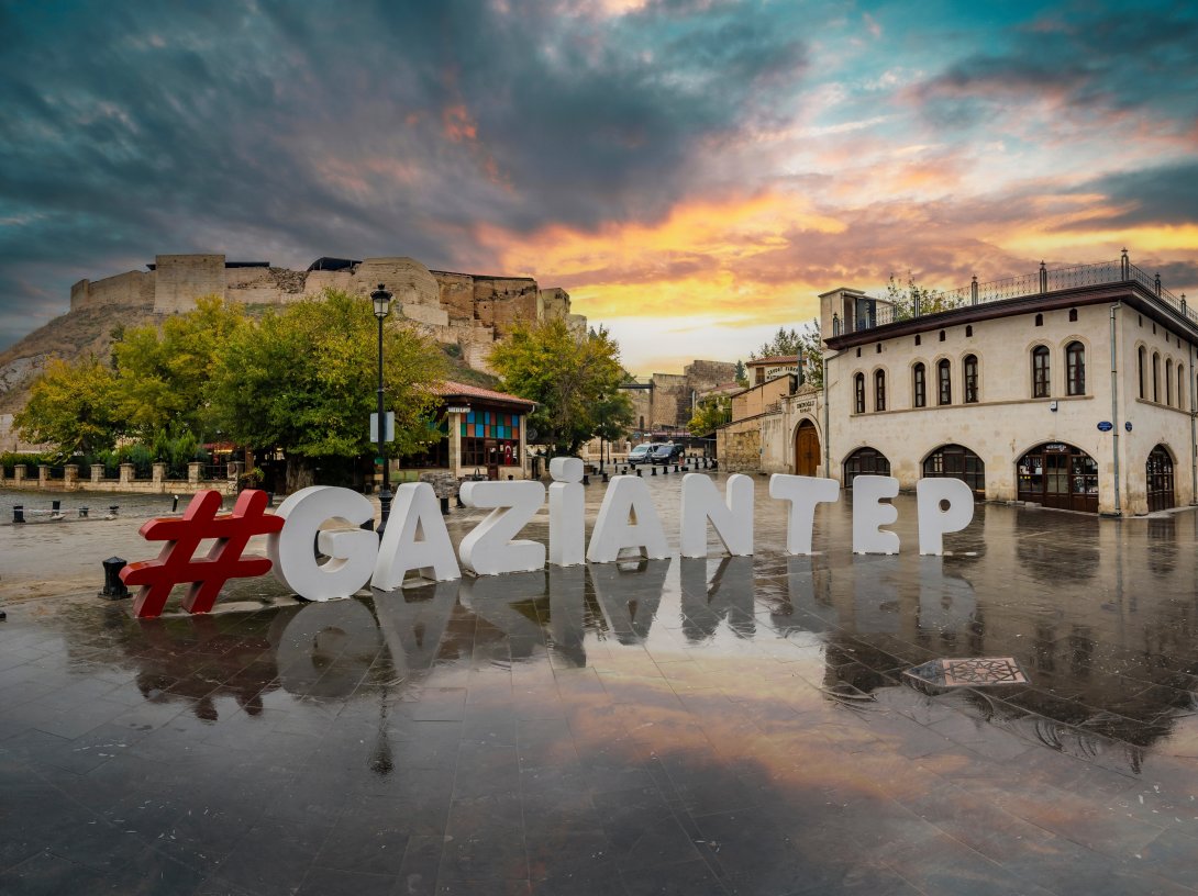 The Gaziantep city logo stands in the foreground with the historic Gaziantep Castle overlooking the city in Gaziantep, southeastern Türkiye, Nov. 16, 2018. (Shutterstock Photo)