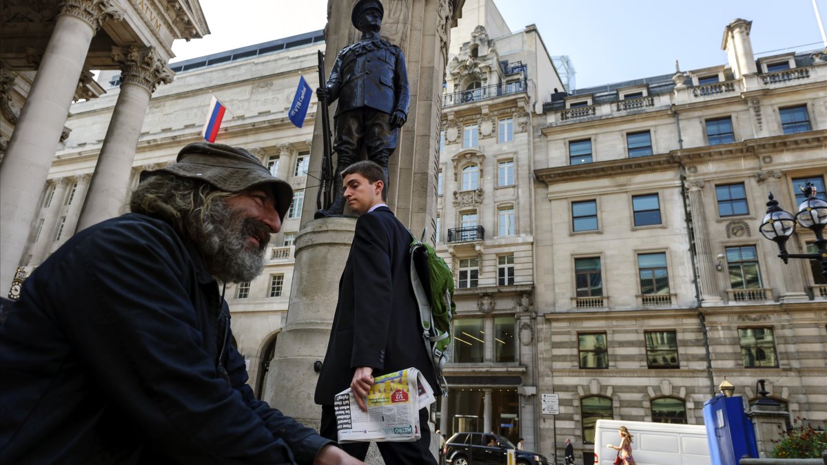 A worker in a jacket and tie glances at a beggar outside the Royal Exchange in London's financial district, known as the City, which now houses luxury shops, U.K., April 15, 2016. (Getty Images Photo)