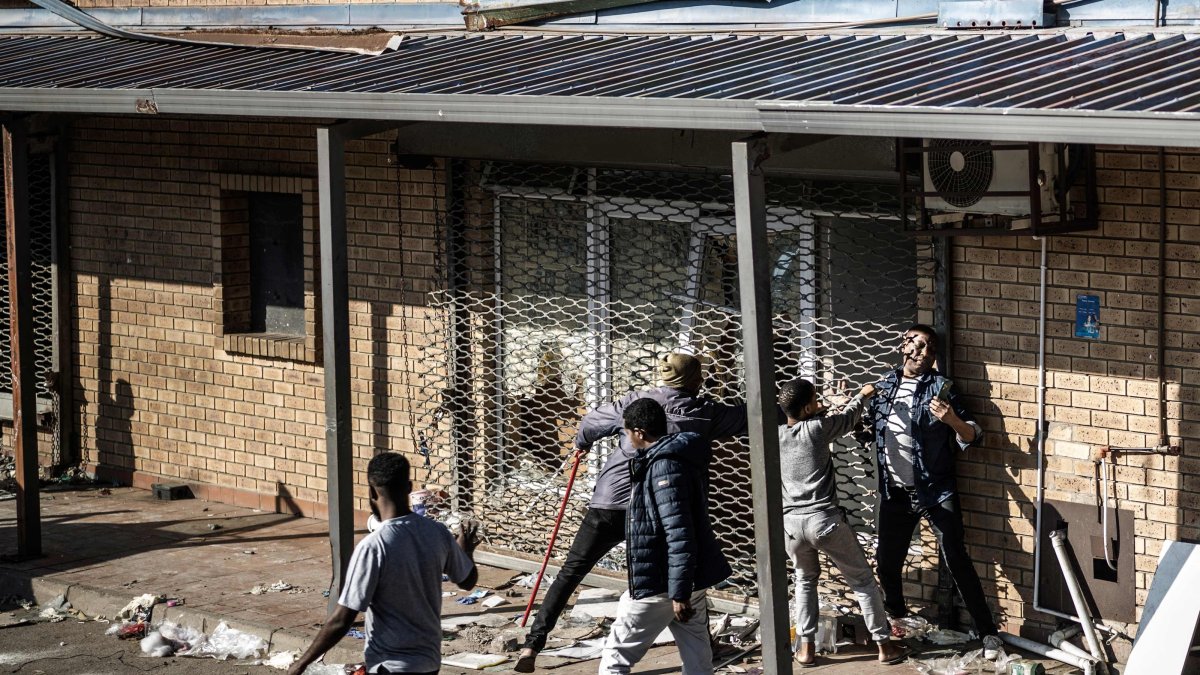 A man tries to squeeze past a metal rolling shutter of a shop that has been looted overnight, Durban, South Africa, July 1, 2026. (AFP Photo)