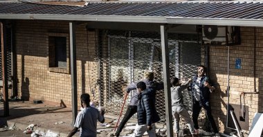 A man tries to squeeze past a metal rolling shutter of a shop that has been looted overnight, Durban, South Africa, July 1, 2026. (AFP Photo)