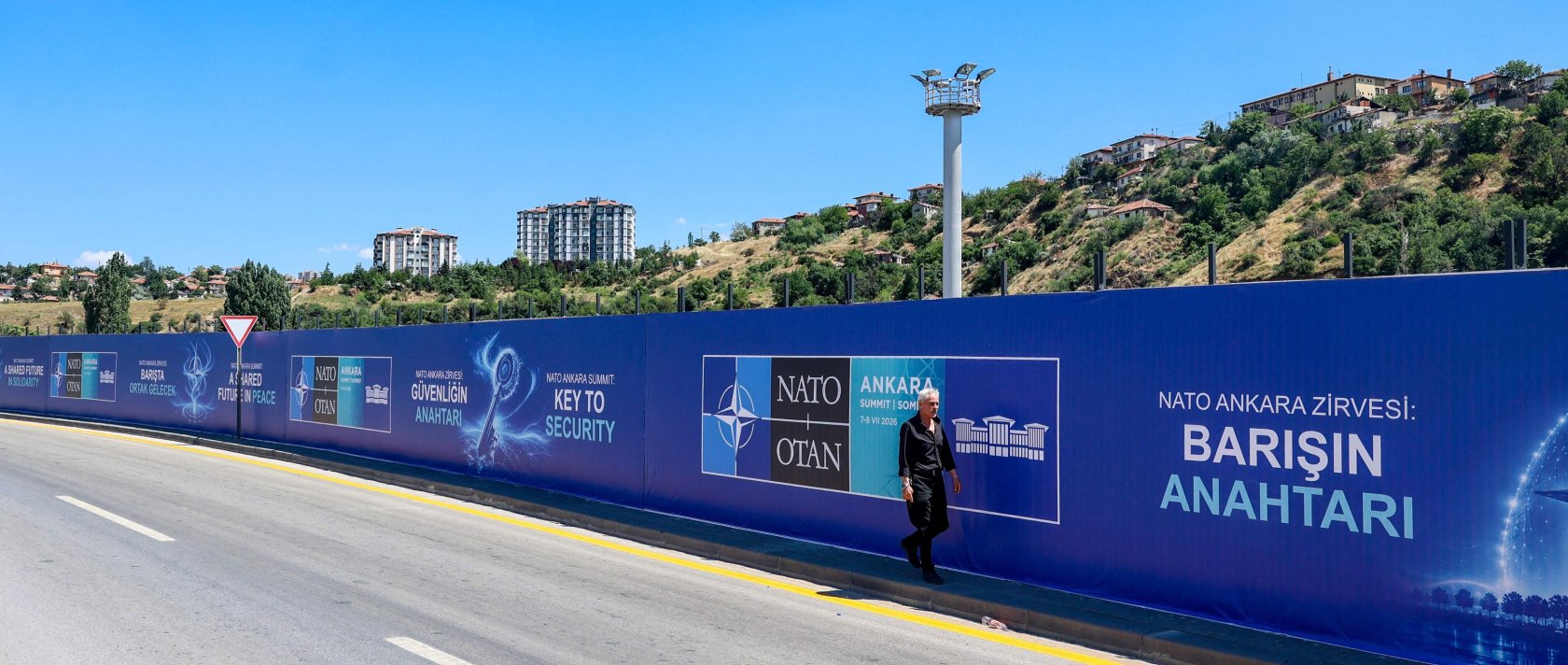 A local resident walks past billboards with the slogans “Key to Peace,” “Key to Security” and “Shared Future in Peace,” displayed along the boulevard on the protocol route ahead of the NATO summit, Ankara, June 26, 2026. (AFP Photo)