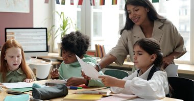 An English teacher passes papers to students. (Shutterstock Photo)