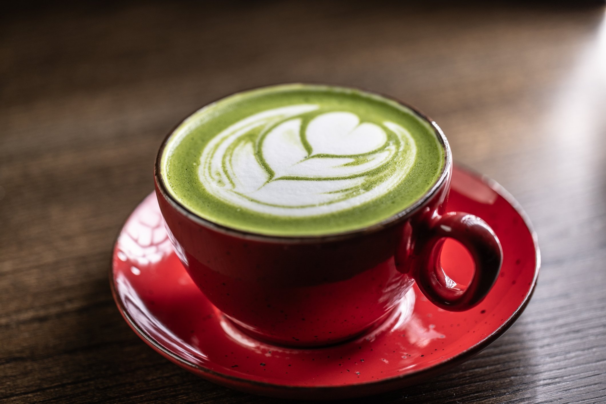 A cup of matcha latte with green milk foam on a wooden table at a cafe. (Getty Images Photo)