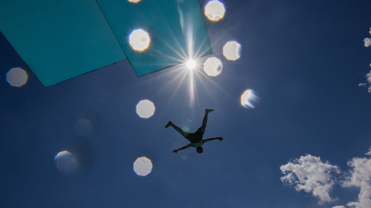A person jumps off the diving platform at the Stadionbad public swimming pool on a hot, sunny day in Cologne, Germany, Thursday, June 18, 2026. (Rolf Vennenbernd/dpa via AP)