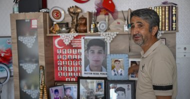 Necmi Perçin poses next to photos of his son Resul at his home, Ankara, Türkiye, July 10, 2026. (AA Photo)