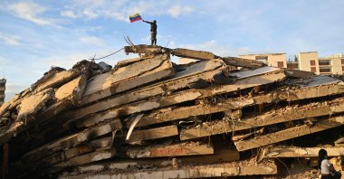 A volunteer waves a Venezuelan flag atop the rubble of the collapsed Obras del Poder Popular (OPP) building in Caraballeda, La Guaira state, Venezuela, July 12, 2026. (AFP Photo)