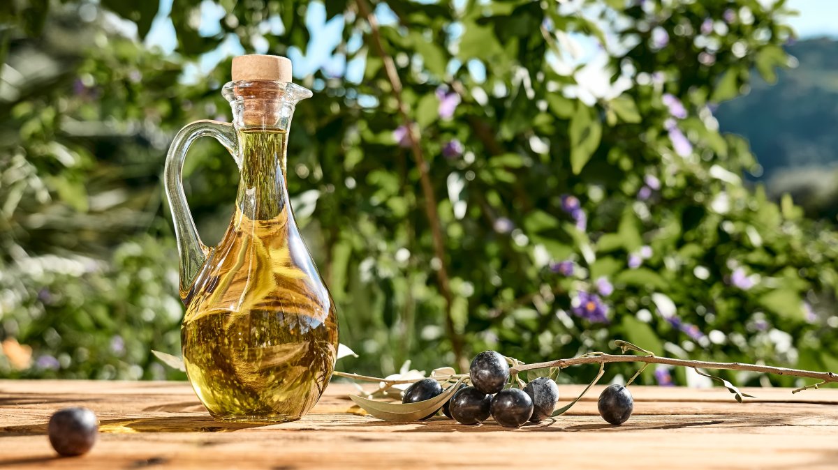 A bottle of extra virgin olive oil and an olive branch on a wooden table in an olive grove. (Shutterstock Photo)