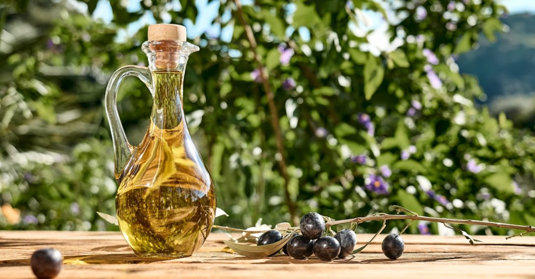 A bottle of extra virgin olive oil and an olive branch on a wooden table in an olive grove. (Shutterstock Photo)