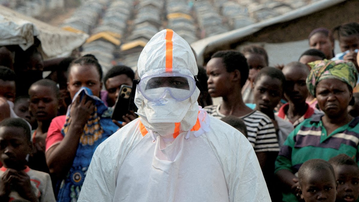 A health worker in personal protective equipment stands near displaced people waiting for the burial of suspected Ebola victims at the Kigonze displaced persons camp, in Bunia, eastern DR Congo, June 18, 2026. (Reuters Photo)