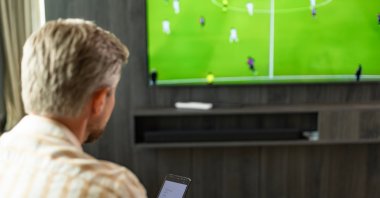 A man uses a smartphone betting app while watching a football match. (Shutterstock Photo)