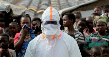 A health worker in personal protective equipment stands near displaced people waiting for the burial of suspected Ebola victims at the Kigonze displaced persons camp, in Bunia, eastern DR Congo, June 18, 2026. (Reuters Photo)