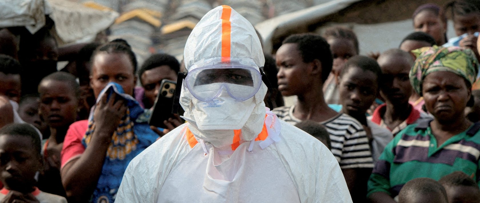 A health worker in personal protective equipment stands near displaced people waiting for the burial of suspected Ebola victims at the Kigonze displaced persons camp, in Bunia, eastern DR Congo, June 18, 2026. (Reuters Photo)