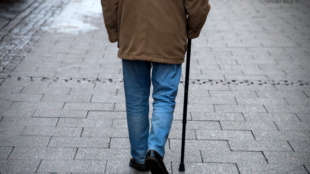 An elderly man walks in the street with a walking stick. (Shutterstock Photo)