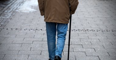 An elderly man walks in the street with a walking stick. (Shutterstock Photo)