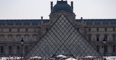 Tourists walk past the Louvre Museum and the Pyramide du Louvre, central Paris, France, July 18, 2026. (AFP Photo)