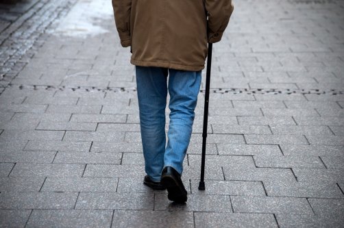 An elderly man walks in the street with a walking stick. (Shutterstock Photo)