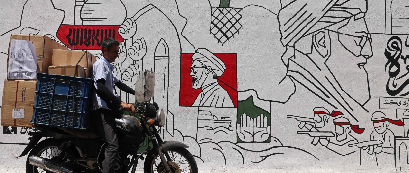 A motorist parks his bike in front of a wall mural along the street in Tehran, Iran, July 21, 2026. (AFP Photo)