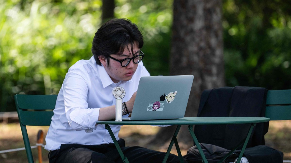 A man uses an electric fan to cool himself down while looking at his laptop in the shade, Tokyo, Japan, July 22, 2026. (AFP Photo)