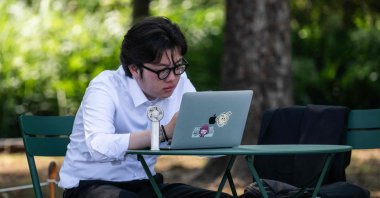 A man uses an electric fan to cool himself down while looking at his laptop in the shade, Tokyo, Japan, July 22, 2026. (AFP Photo)