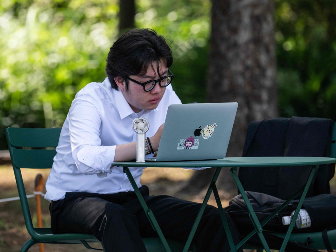 A man uses an electric fan to cool himself down while looking at his laptop in the shade, Tokyo, Japan, July 22, 2026. (AFP Photo)