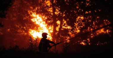 A firefighter sprays water on a burning forest close to a residential area during a wildfire near Lege-Cap-Ferret, France, July 23, 2026. (AFP Photo)