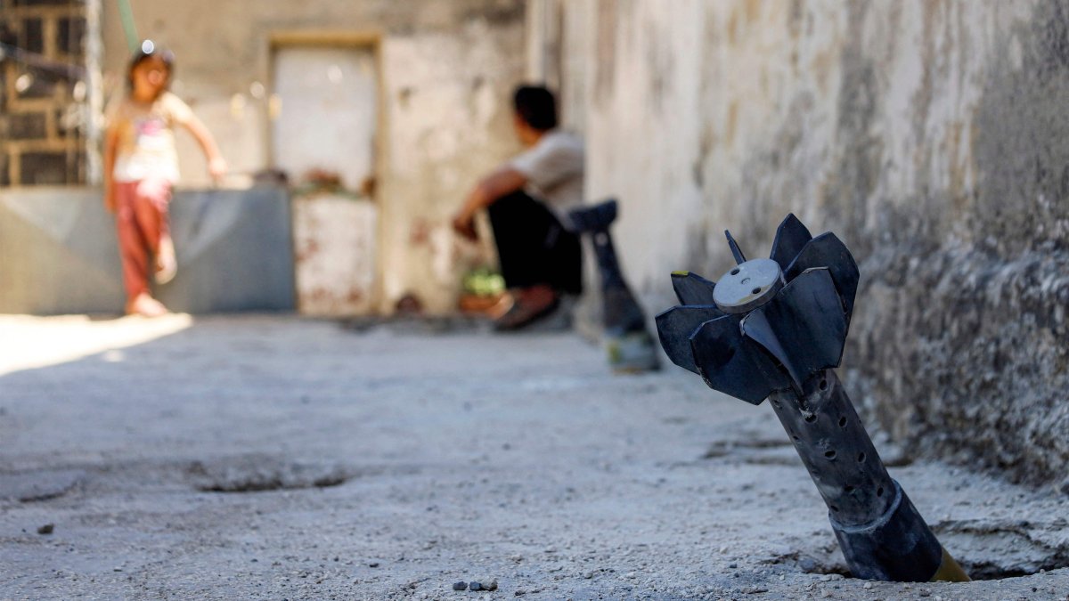 This file photo shows a man speaking with a child while sitting near an unexploded artillery shell that fell during overnight Israeli bombardment on the village of Abidin in Daraa, southeastern Syria, June 29, 2026. (AFP Photo)