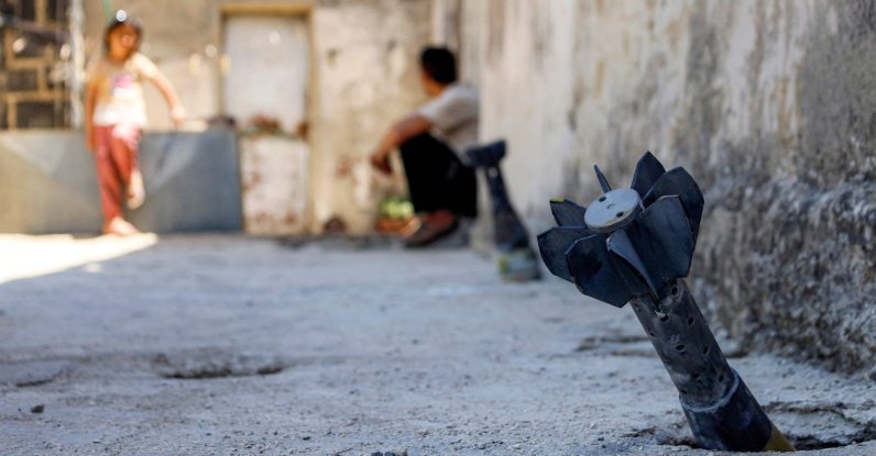 This file photo shows a man speaking with a child while sitting near an unexploded artillery shell that fell during overnight Israeli bombardment on the village of Abidin in Daraa, southeastern Syria, June 29, 2026. (AFP Photo)