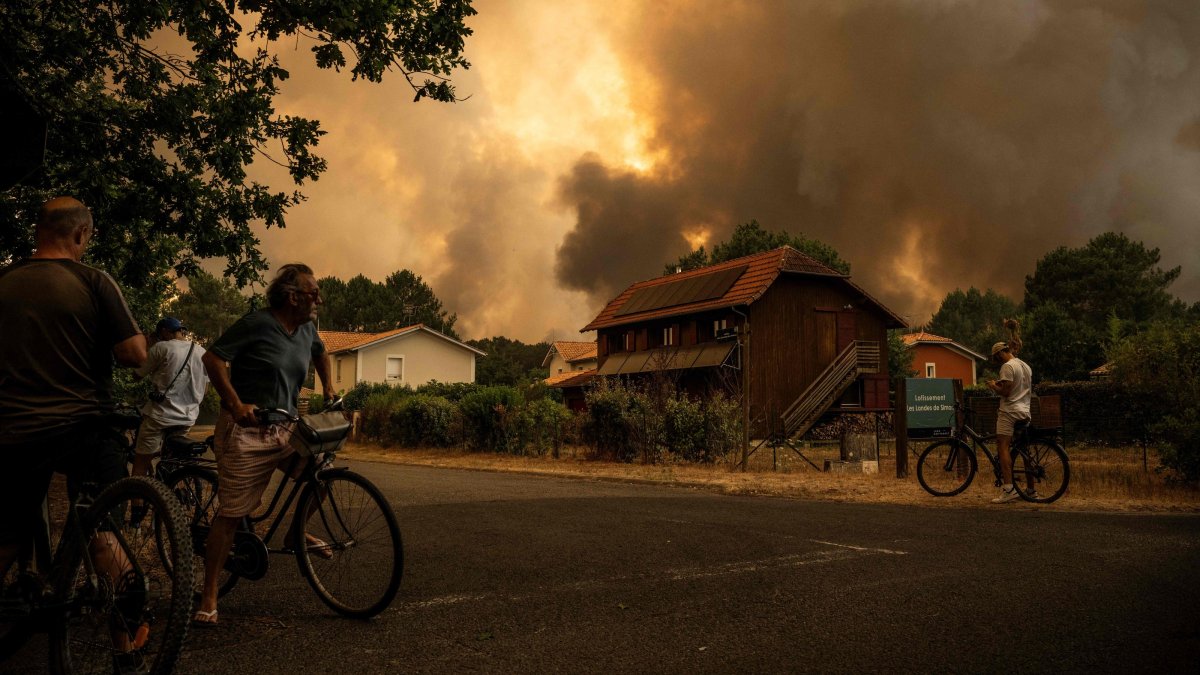Residents on their bicycles look at smoke rising behind a residential area during a wildfire near Lege-Cap-Ferret, southwestern France, July 23, 2026. (AFP Photo)