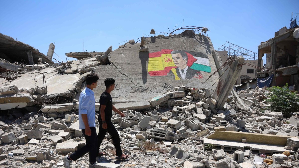 Displaced Palestinian men walk past a mural painted on the remains of a building destroyed during the Israeli bombardment of the Gaza Strip, by Gazan artist Ubay Karim al-Qurshali, also known as Ubay Karim, depicting Spain's Prime Minister Pedro Sanchez sandwiched between his national flag (L) and the Palestinian flag, in Gaza City, July 27, 2026. (AFP Photo)