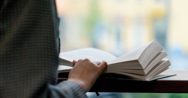 A person reading a book in front of the window. (Shutterstock Photo)