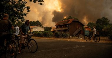 Residents on their bicycles look at smoke rising behind a residential area during a wildfire near Lege-Cap-Ferret, southwestern France, July 23, 2026. (AFP Photo)