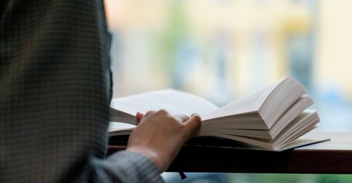 A person reading a book in front of the window. (Shutterstock Photo)