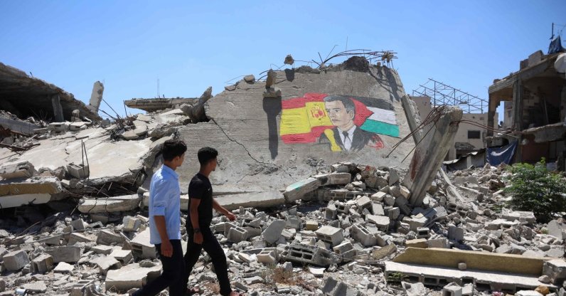 Displaced Palestinian men walk past a mural painted on the remains of a building destroyed during the Israeli bombardment of the Gaza Strip, by Gazan artist Ubay Karim al-Qurshali, also known as Ubay Karim, depicting Spain's Prime Minister Pedro Sanchez sandwiched between his national flag (L) and the Palestinian flag, in Gaza City, July 27, 2026. (AFP Photo)