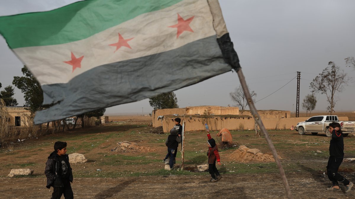 Children walk near a Syrian flag at a checkpoint in the town of Sarin, Hassakeh province, eastern Syria, Feb. 2, 2026. (AP Photo)