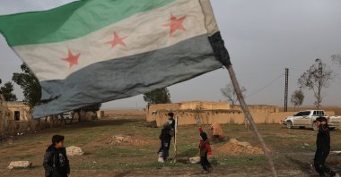 Children walk near a Syrian flag at a checkpoint in the town of Sarin, Hassakeh province, eastern Syria, Feb. 2, 2026. (AP Photo)