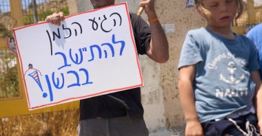 A Jewish extremist holds a sign that reads "It's about time to settle in the Bashan," in the Israeli-occupied Golan Heights, July 21, 2026. (AP Photo)