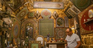 Syrian artisan Eyman Said works inside his workshop displaying traditional wood relief artworks in the historic souks of Aleppo, Syria, July 28, 2026. (AA Photo)