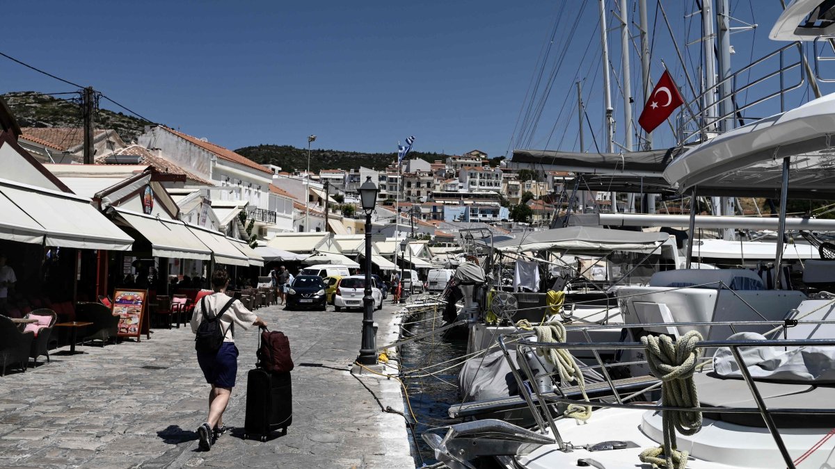 A tourist from Türkiye walks with a suitcase next to sailboats with a Turkish flag in Pythagorion village, Samos island, Greece, July 24, 2026. (AFP Photo)