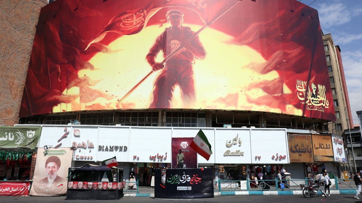 A man holds Iran's national flag in front of a large political billboard at Valiasr Square in Tehran, Iran, Aug. 1, 2026. (EPA Photo)