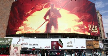 A man holds Iran's national flag in front of a large political billboard at Valiasr Square in Tehran, Iran, Aug. 1, 2026. (EPA Photo)