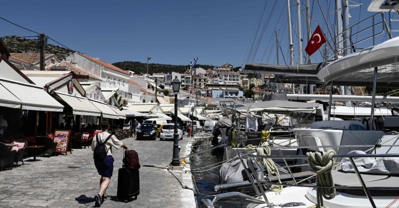 A tourist from Türkiye walks with a suitcase next to sailboats with a Turkish flag in Pythagorion village, Samos island, Greece, July 24, 2026. (AFP Photo)