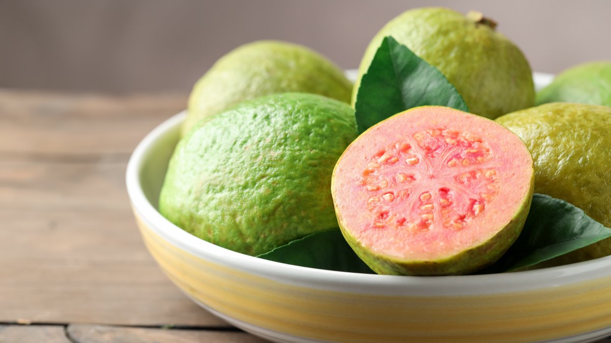 Fresh guava fruits in bowl on wooden table, closeup