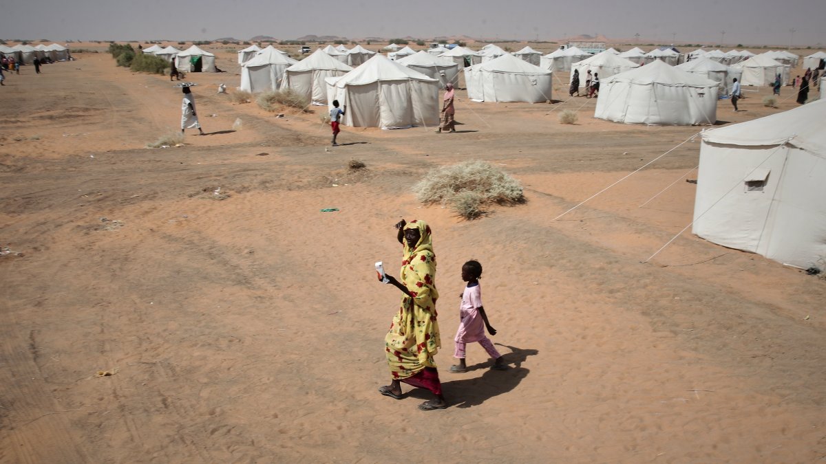 A woman and a child, displaced from North Darfur's capital, el-Fasher or other conflict-affected areas, walk in the newly established el-Afadh camp in al Dabbah, Northern State, Sudan, Nov. 13, 2025. (AP Photo)