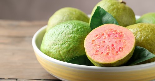 Fresh guava fruits in bowl on wooden table, closeup