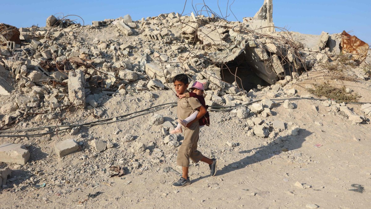 A Palestinian child carries a little girl on his back as he walks past the rubble of destroyed buildings in the Jabalia camp for Palestinian refugees in the northern Gaza Strip, Palestine, Aug. 2, 2026. (AFP Photo)