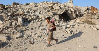 A Palestinian child carries a little girl on his back as he walks past the rubble of destroyed buildings in the Jabalia camp for Palestinian refugees in the northern Gaza Strip, Palestine, Aug. 2, 2026. (AFP Photo)