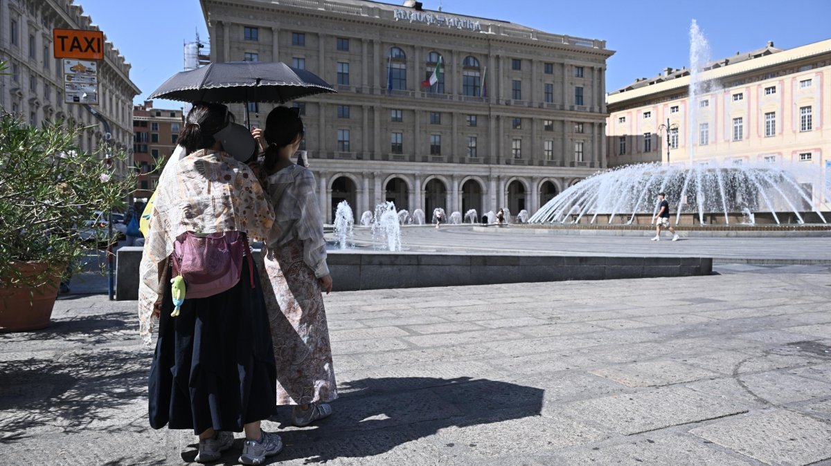 Tourists seek shelter from the heat under an umbrella on Piazza De Ferrari in Genoa, Italy, Aug. 6, 2026. (EPA Photo)