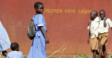 Students play in front of a wall painted with a slogan supporting children's rights outside of their school, district of Mukono, Uganda, July 20, 2009. (Getty Images Photo)