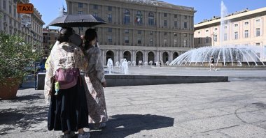 Tourists seek shelter from the heat under an umbrella on Piazza De Ferrari in Genoa, Italy, Aug. 6, 2026. (EPA Photo)